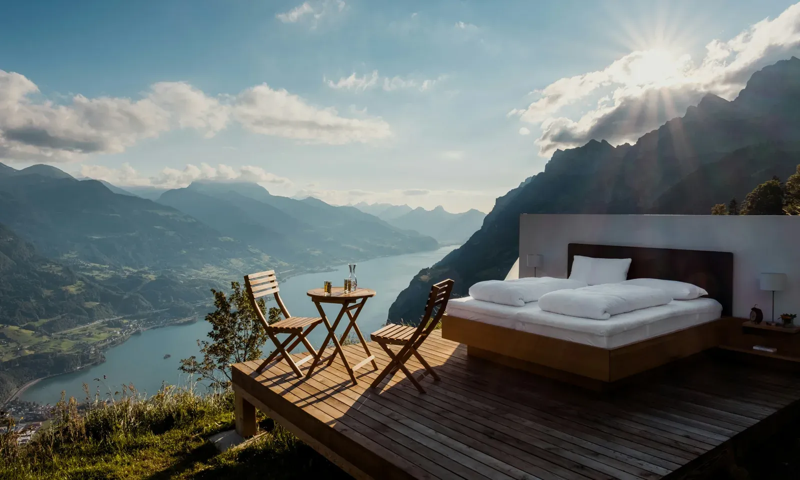 Bed and table on a wooden deck overlooking a mountain valley at sunrise