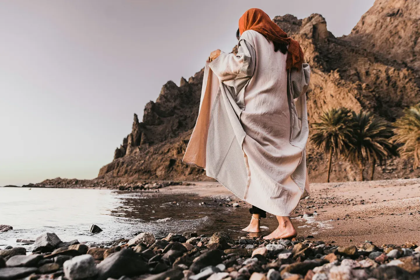 Figure in a robe walking a rocky shoreline