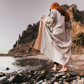 Figure in a robe walking a rocky shoreline