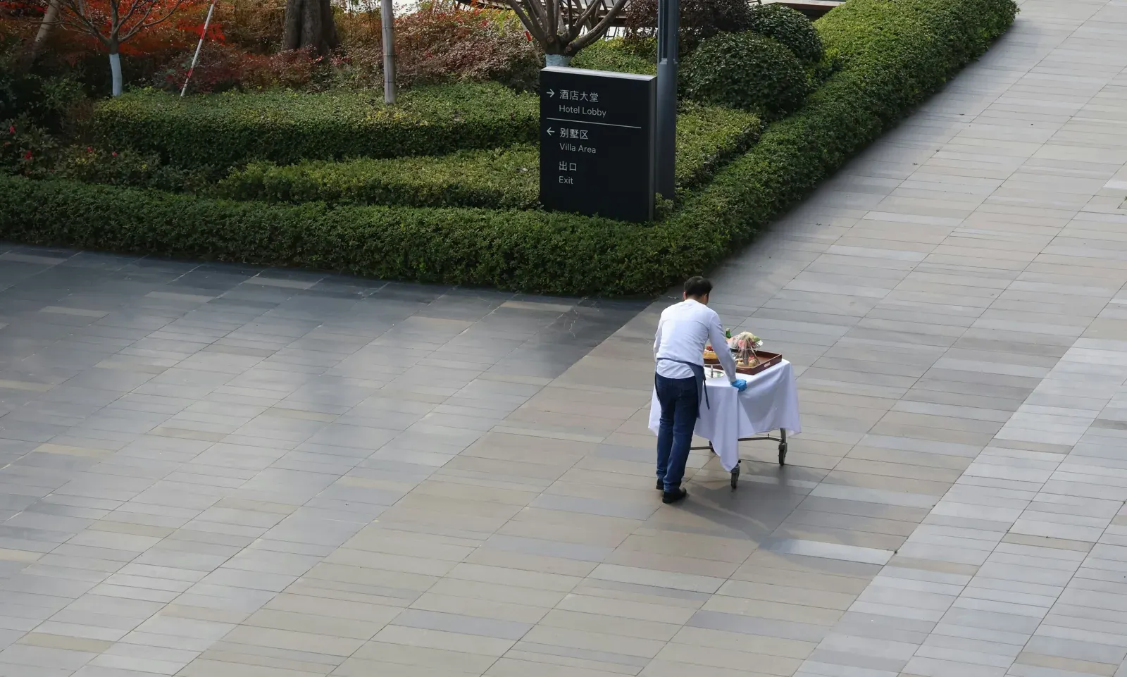 Hotel concierge wheeling a service cart past directional signage at a luxury resort