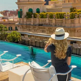Sun-hat figure at a rooftop pool over a cityscape