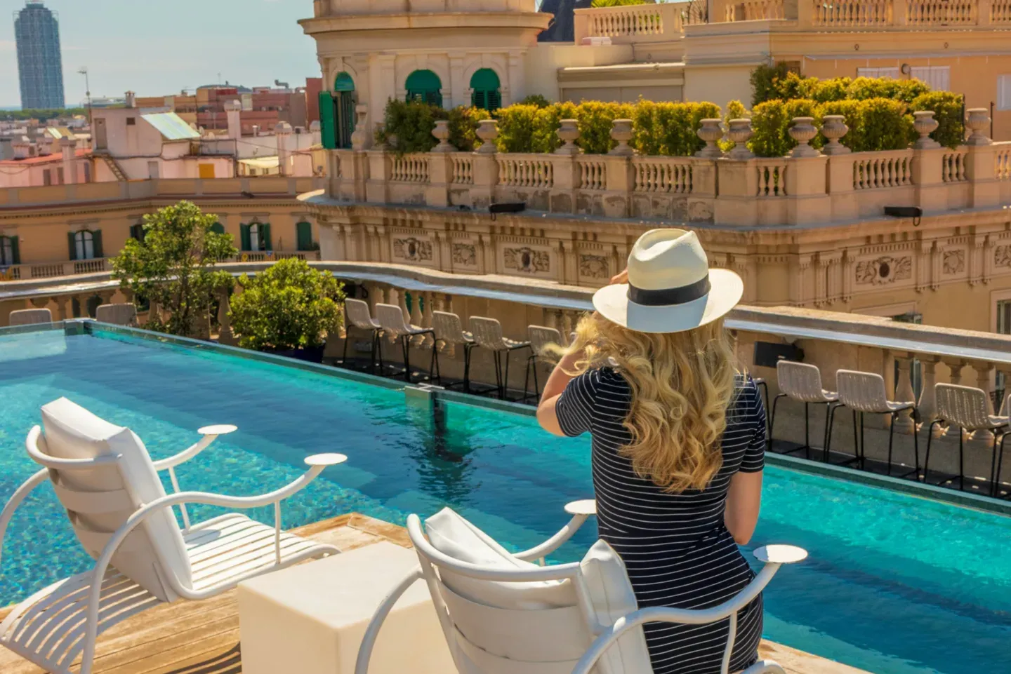 Sun-hat figure at a rooftop pool over a cityscape