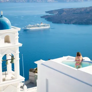 Santorini bell tower above a plunge pool with cruise ship beyond