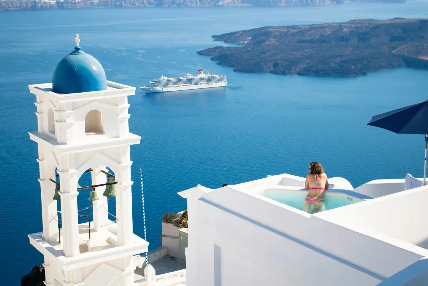 Santorini bell tower above a plunge pool with cruise ship beyond